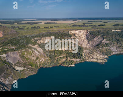 Drone aérien vue de carrière abandonnée avec le lac est apparu sur le fond, la surface de miroir de l'eau dans la soirée ensoleillée, envahie par la forêt avec sh Banque D'Images