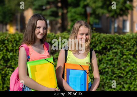 Deux jeunes filles adolescente lycéenne en été dans le parc après l'école. Mains tenant un dossier d'ordinateurs portables derrière les sacs à dos. Concept à l'école. Les émotions de bonheur et de sourires sur le visage. Banque D'Images