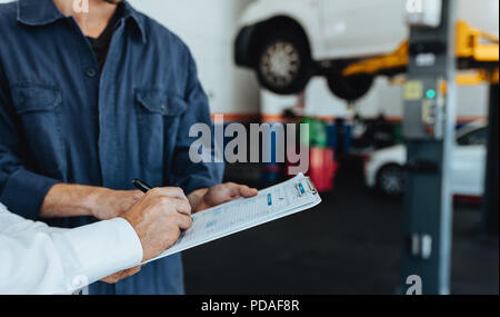 En mécanicien signe sur le document à partir de client dans un garage. Mains de client de service de voiture documents signature après avoir réparé sa voiture. Banque D'Images