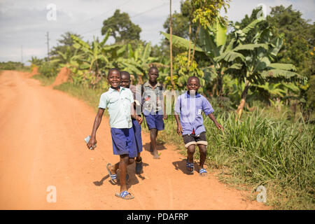 Heureux les enfants de l'école courir vers le bas une route poussiéreuse dans le district de Mukono, en Ouganda. Banque D'Images