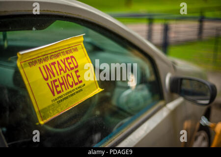Détail d'un panneau d'avertissement sur la fenêtre d'un véhicule non taxées avec un collier sur la roue avant Banque D'Images