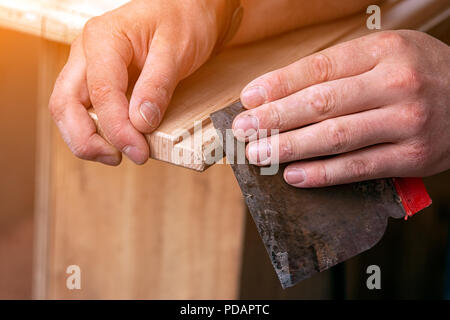 Close-up un charpentier de vêtements de travail de restauration d'un bois avec une spatule sur une table en bois. L'homme travailleur de la construction d'une cale de bois de plâtrage Banque D'Images