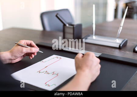 L'homme assis à table et est titulaire d'stylo dans la main gauche. Il y a des feuille de papier avec un tableau sur la table de négociation. Concept photo. Banque D'Images