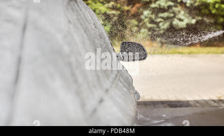 Shampoing mousse et une pulvérisation d'eau tombant sur le rétroviseur d'une voiture lavés dans self service carwash. L'accent de chute uniquement, à gauche, la place pour le texte. Banque D'Images
