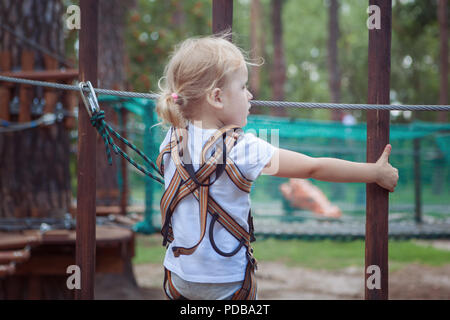 Petite fille blonde surmonte un obstacle dans un cable park. Banque D'Images