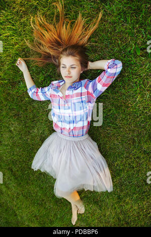 Portrait of young Beautiful woman with red hair malpropre lying on grass en chemise à carreaux et tulle tutu jupe. Vue du dessus top frais généraux. Conc Banque D'Images