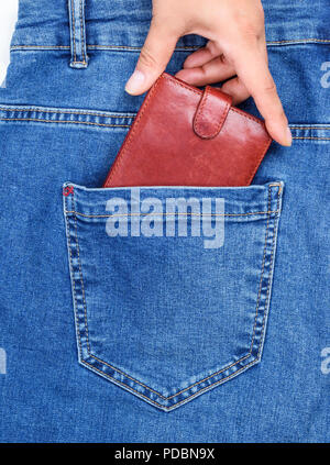 Sac à main en cuir marron dans la poche arrière de jeans et d'une main humaine, il tire une image complète Banque D'Images