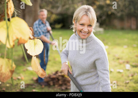 Portrait souriant, confiant mature woman ratissage des feuilles en automne arrière-cour Banque D'Images