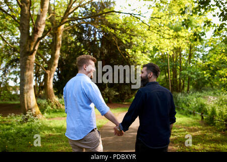 Homme affectueux gay couple holding hands in sunny park Banque D'Images