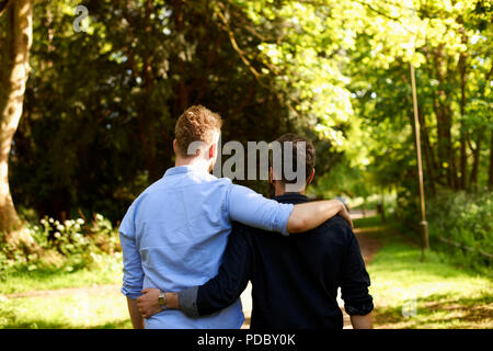 Homme affectueux gay couple hugging, randonnée pédestre à sunny park Banque D'Images