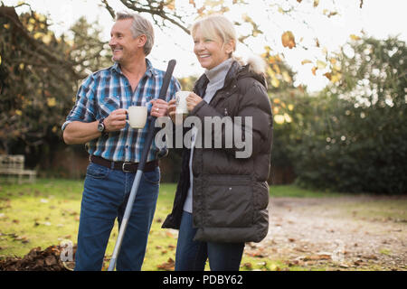 Mature couple drinking coffee et raking autumn leaves in backyard Banque D'Images