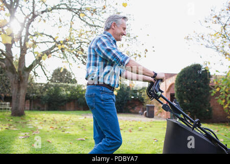 Man avec tondeuse à gazon en mouvement à l'automne jardin Banque D'Images