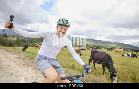 Portrait de l'homme insouciant avec caméra portable randonnée cycliste sur route de terre le long des pâturages de vache Banque D'Images