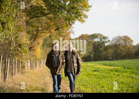 Mature couple walking arm in arm sous le soleil, l'automne rural field Banque D'Images