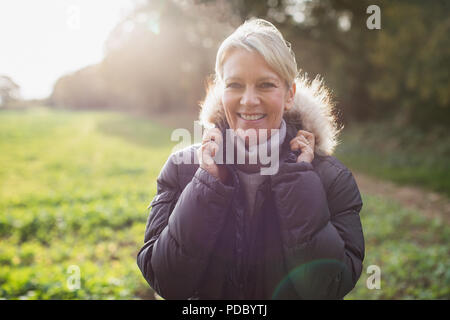 Portrait souriant, confiant mature woman in parka à sunny park Banque D'Images