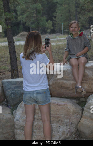 Woman taking photo, avec téléphone cellulaire, de jeune fille, habillé avec rose entre, assis dehors sur la roche. Modèle vertical et les deux libérés Banque D'Images