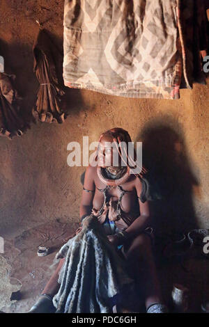 Femme Himba Otjikandero, à la maison, village du nord de la Namibie. Coller à l'ocre rouge est utilisé pour nettoyer la peau et aider à protéger contre les piqûres de moustiques.. Banque D'Images