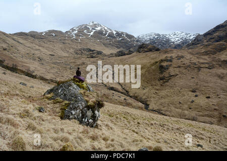Un solo female hiker revient sur les Highlands écossais alors qu'elle repose sur un rocher au cours d'une randonnée dans la péninsule de Knoydart, Ecosse, Royaume-Uni. Banque D'Images