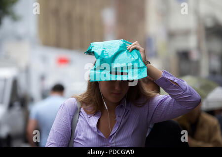 London,UK,9 août 2018,le temps humide typiquement britannique reprend à Londres. Une dame couvre sa tête avec un sac en plastique qu'une protection contre la pluie à Waterloo. La prévision est pour la pluie pour le reste de la journée. Larby Keith Crédit/Alamy Live News Banque D'Images