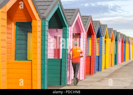 Jogger passant devant des cabanes de plage colorées sur la plage de Saltburn.Saltburn au bord de la mer, Yorkshire du Nord, Angleterre.ROYAUME-UNI Banque D'Images