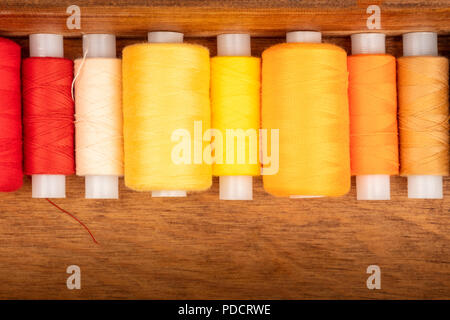 Une photo prise à la verticale du vibrant jaune et orange des bobines de fils à coudre dans une boîte en bois Banque D'Images