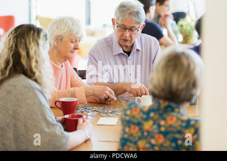 Senior friends assemblage jigsaw puzzle et boire du thé à table dans un centre communautaire Banque D'Images