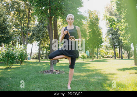 Attractive Woman practicing yoga en posture de l'arbre et faire son avec bol chantant tibétain dans park Banque D'Images