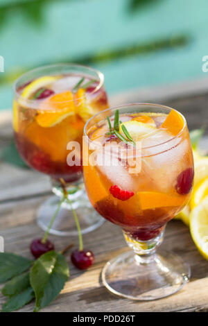 Vin rafraîchissant maison sangria ou punch aux fruits dans les verres. Sangria cocktails de fruits frais, de baies et de romarin. Sur une table rustique en bois, Banque D'Images