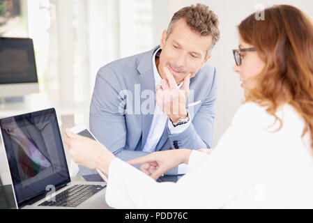 Businesswoman using digital tablet while sitting at office desk avec son collègue de la pensée et d'avoir la discussion. Le travail d'équipe à l'office. Banque D'Images