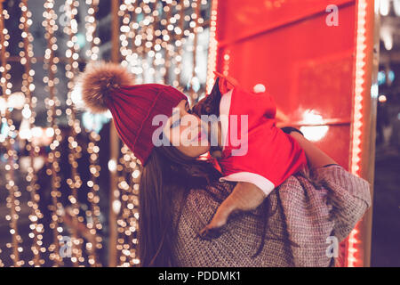 Belle jeune femme brune avec bouledogue français bénéficiant de Noël ou Nouvel An nuit sur une rue de la ville. Banque D'Images