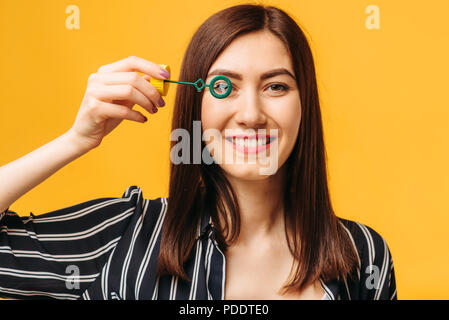 Femme heureuse avec bulle de savon, fond jaune Banque D'Images