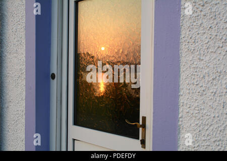 Un coucher de soleil sur le Loch Nevis reflétée sur une vitre de porte dans la ville de Inverie dans la péninsule de Knoydart, dans les highlands, Ecosse, Royaume-Uni. Banque D'Images