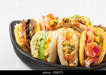 Arepas avec différents fourrages servis dans un plat de céramique noire sur fond blanc Banque D'Images