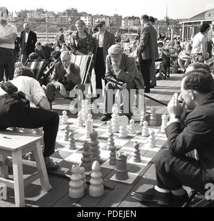 Années 1950, historique, les hommes assis sur des chaises longues à l'extérieur, jouant un jeu d'échecs de pont sur le plancher en bois d'une station pier, England, UK. Banque D'Images