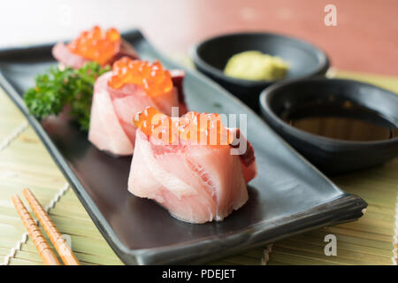 Oeufs de saumon sur Hamachi sushi sur la plaque noire avec la sauce japonaise et vert feuille décor, la nourriture Japonaise, Close up à sushi. Banque D'Images
