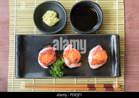 Oeufs de saumon sur Hamachi sushi sur la plaque noire avec la sauce japonaise et vert feuille décor, la nourriture Japonaise, sushi à vue de dessus. Banque D'Images