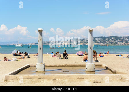 Les douches de plage de plage de la Pointe Rouge à Marseille, France, avec des gens de soleil et planche à voile à l'arrière-plan par une journée de printemps ensoleillée et chaude. Banque D'Images