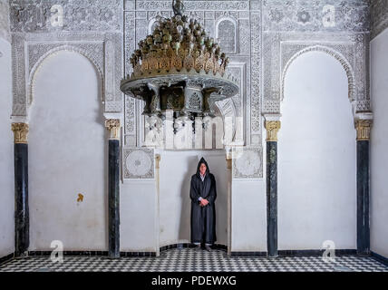 Fes, Maroc - 11 mai 2013 : l'homme dans l'habillement berbère dans une alcôve de la cour intérieure du 14ème siècle, El Attarine médersa de Fès, Maroc Banque D'Images