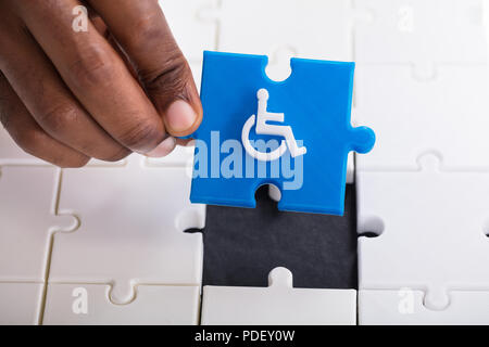 La main qui tient un morceau de puzzle bleu avec des personnes handicapées l'icône en fauteuil roulant Banque D'Images