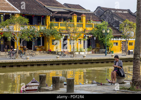 Fille asiatique assis près d'Hoi An à la rivière à son téléphone cellulaire. Photo de presse Banque D'Images