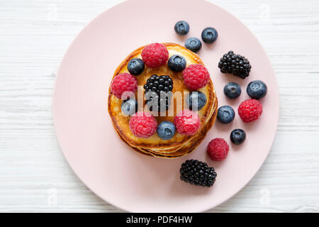 Crêpes aux fruits rouges sur une plaque rose sur table en bois blanc, vue du dessus. Banque D'Images