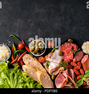 L'antipasto set plateau sur fond noir en noir. La viande fumée à froid avec plaque,saucisse jambon tranché, bacon, olives, pain, fromage et d'herbes. Variété de hors-d'avec copie espace. Vue de dessus ou de télévision. Square Banque D'Images