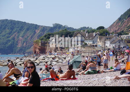 Personnes bronzer et se détendre sur la plage de Sidmouth. Chaumières et de falaises de grès dans la distance. L'est du Devon, Royaume-Uni. Août, 2018. Banque D'Images