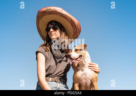 Belle fille de Mexican Hat déguisé en bandit de gangster avec chien dans cool lunettes de soleil. Personne de sexe féminin en chapeau sombrero et bandana posant avec pupp Banque D'Images