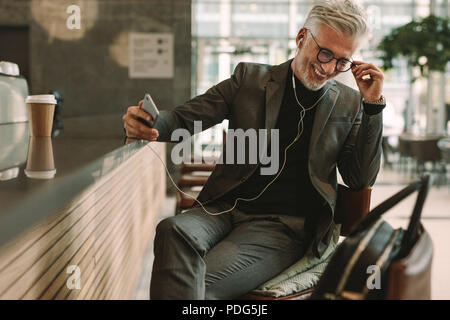 Businessman in coffee shop d'écouter de la musique sur les écouteurs. Mature businessman sitting at cafe des écouteurs et la tenue d'un téléphone mobile. Banque D'Images