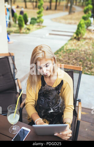 Belle et bonne blonde woman with tablet en bénéficiant d'un café bar avec son adorable bouledogue français. Banque D'Images