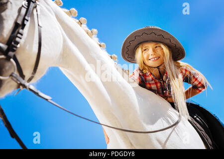 Cute smiling girl petting horse racing blanc alors qu'il était assis sur lui Banque D'Images