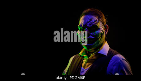 Portrait d'un homme bien habillé portant un masque de clown maléfique avec suture du crâne et un miroir en dessous. L'horreur et le thème de l'Halloween, tourné avec theatric Banque D'Images