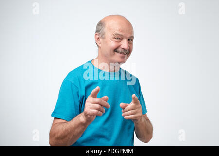 Excitée mature man in blue shirt pointer du doigt et isolée de l'appareil photo sur un fond blanc Banque D'Images