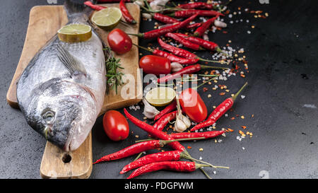 Dorado frais sur une planche à découper en bois. Herbes aromatiques, de lime, les tomates cerise, le sel, le paprika et les épices. Close-Up Banque D'Images